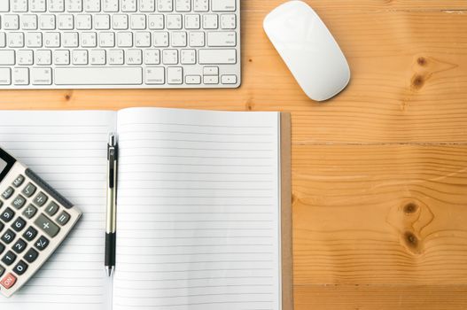 Top view workspace with blank notebook,pen,calculator keyboard and mouse on wooden table background.