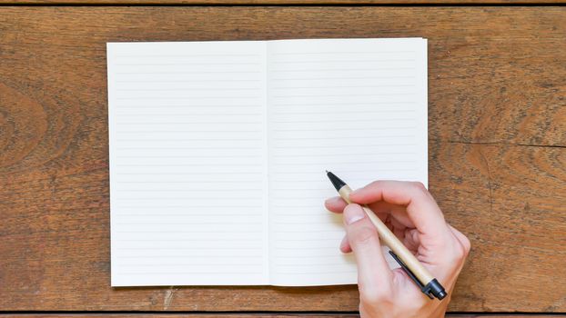 Man hands with pen writing on empty notepad over wooden table.