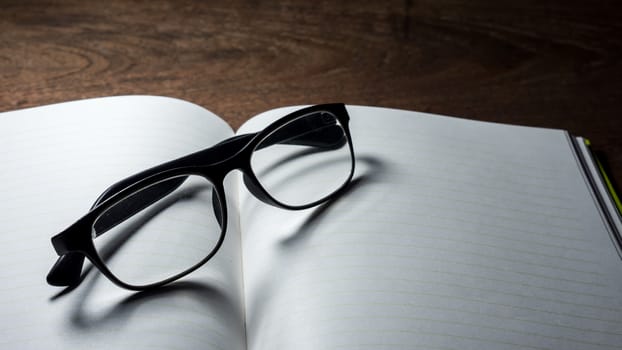 Blank notebook with  glasses on wooden table.