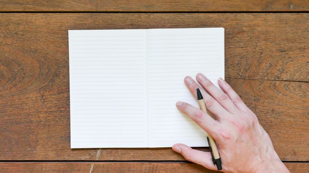 Man hands with pen writing on empty notepad over wooden table.