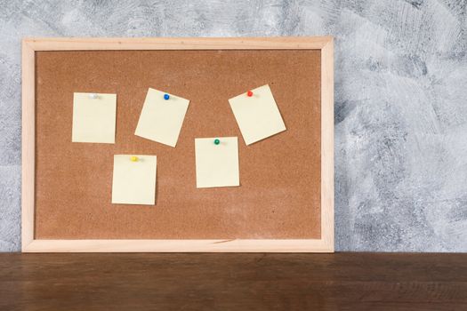 Blank papers pin up on cork board over wooden table with textured background.