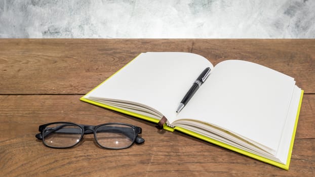 Blank notebook with pen and glasses on wooden table.