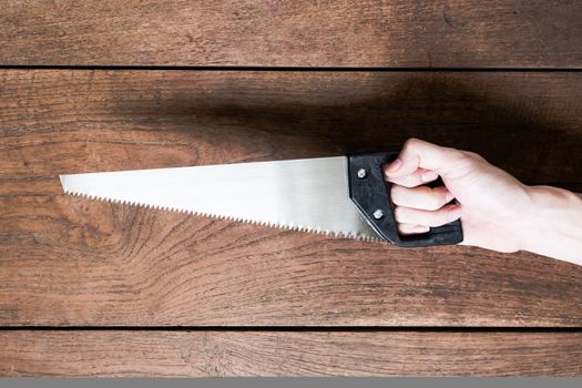 Hand holding saw on wooden table background.