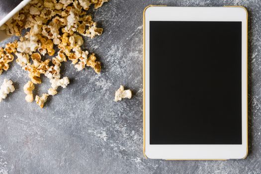White tablet touch computer gadget with popcorn on grunge background.