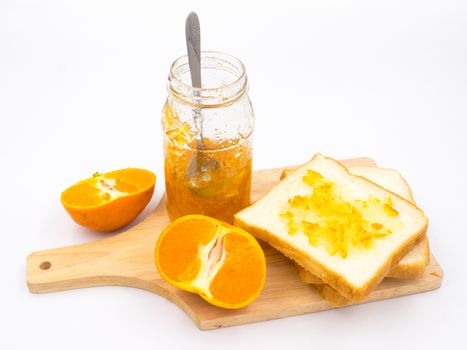 Fresh orange with orange jam in glass jar and  bread on wooden tray over white background.