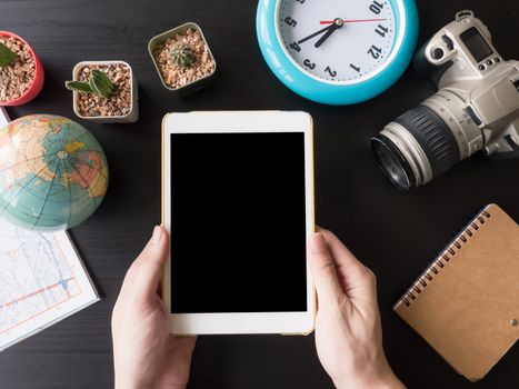 Top view of tablet in hands with camera,cactus,map,globe,clock  and notebook on the office desk.