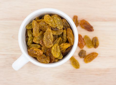 Yellow raisins in cup  on wooden background.