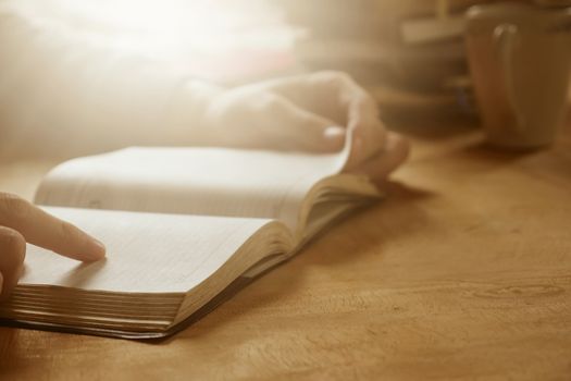 Close up of male hands open a book on wooden desk, Soft focus, Flare sunlight, Vintage tone.