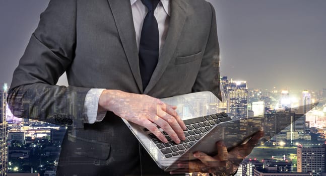 Double exposed of  Businessman holding laptop with cityscape.