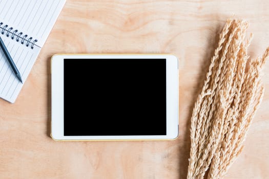 Top view of  notepad, tablet computer, wheat ears on wooden table background.
