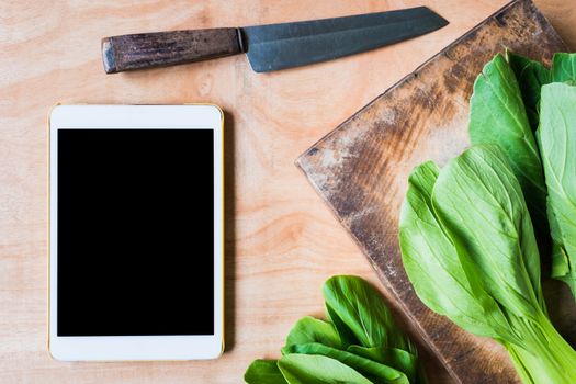 Top view of Bok choy (chinese cabbage) on wooden chopping block with knife and tablet touch computer gadget.