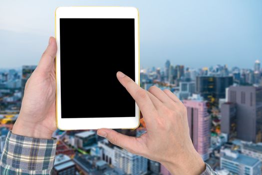 Male hands holding a white tablet touch computer gadget with touch blank black screen on blurred city landscape background.