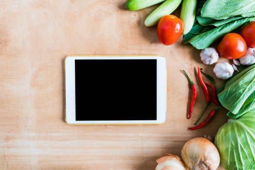 Top view of Fresh vegetables with tablet touch computer gadget on wooden table background.