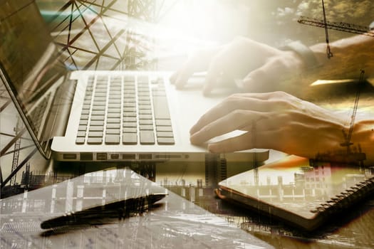 Double exposed of male hands working on laptop with the building construction site.