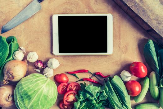 Top view of Fresh vegetables with tablet touch computer gadget on wooden table background.