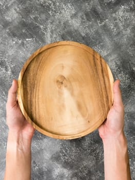 Top view of empty wooden tray with hands on grunge  background.