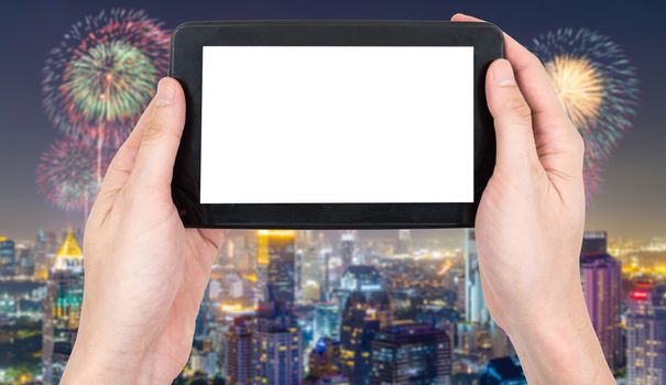 Male hand holding a tablet touch computer gadget with touch blank screen on blurred city landscape and firework background.