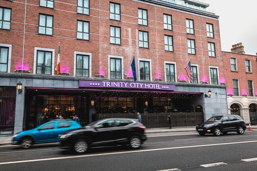 Dublin, Ireland - February 11, 2019: People and cars driving past the facade of the luxurious Trinity City Hotel in the city center on a winter day