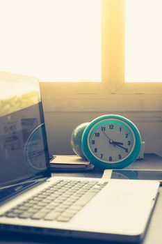 Clock with Laptop on office desk and  
sunshine in afternoon.