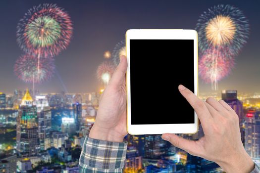 Male hand holding a tablet touch computer gadget with touch blank screen on blurred city landscape and firework background.