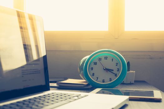 Clock with Laptop on office desk and  
sunshine in afternoon.