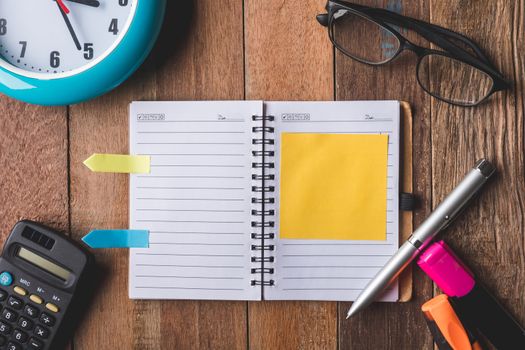 Top view of Notebook with Office supplies,clock and glasses on wooden table background.
