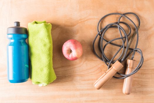 Top view of bottle with towel,apple and skipping rope on wooden table background, Fitness lifestyle concept