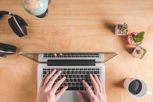 Topview of Male hands woking on laptop with headphone ,cactus,globe and coffee cup on wooden table background.