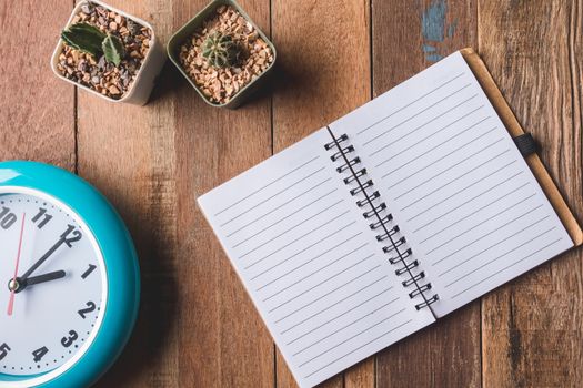 Top view of Blank notebook with clock and cactus on wooden table background.