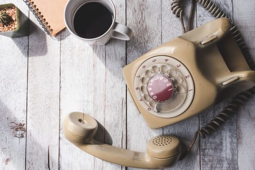 Top view of Old telephone with coffee cup,notebook and cactus on white wooden table background.