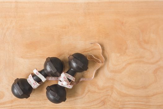 Top view of iron dumbbells with measure tape on wooden table background. Free space for text