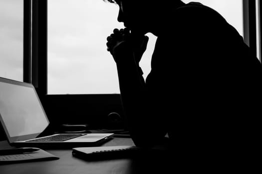 Silhouette image of A man looking at his laptop on the desk.
