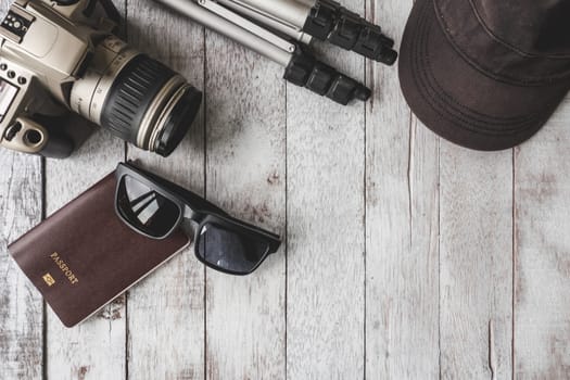 Top view of Camera with tripod,cap,sunglasses and passport on white wooden table background, Travel concept