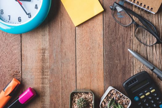 Top view of  Office supplies with clock,glasses and cactus on wooden table background. Free space for text