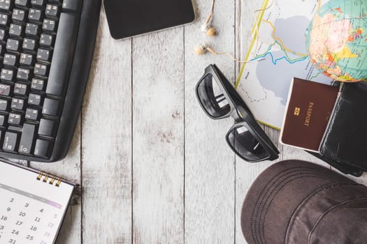Top view of Keyboard with calendar, smartphone, earphones, sunglasses, cap, wallet, passport, map and globe on white wooden table background. Travel concept