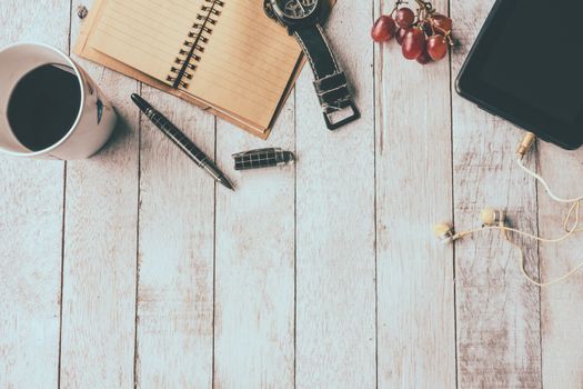 Top view of Coffee cup with notebook,pen,watch,tablet,earphone and grape on white wooden table background, Vintage tone, Free space for text