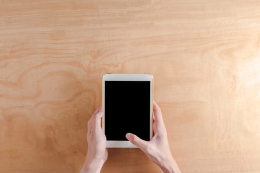 Top view of Male hands holdind tablet touch computer gadget on wooden background.