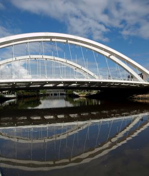 A modern arch bridge for cyclists and pedestrians with reflection in the river