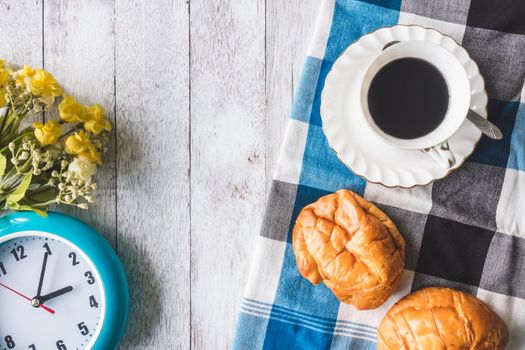 Top view of Coffee cup with bread, tablecloth, flowers and clock on wooden table background