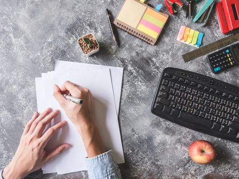 Top view of Male hands writing on paper sheet with Office supplies on Grunge gray background