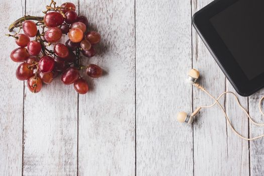Top view of Red grapes with tablet and earphone on white wooden table background. Free space for text