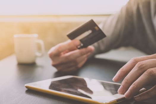 Male hands holding credit card and using Tablet with a cup of coffee on the table, soft focus, flare sun light, Online shopping concept.