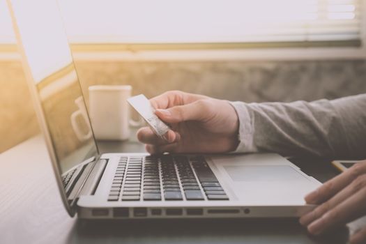 Male hands holding credit card and using Tablet with a cup of coffee on the table, soft focus, flare sunlight, Online shopping concept.