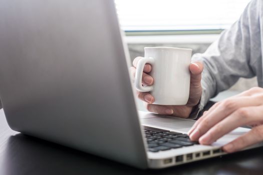 Male hands working on Laptop and holding a cup of coffee on the desk.