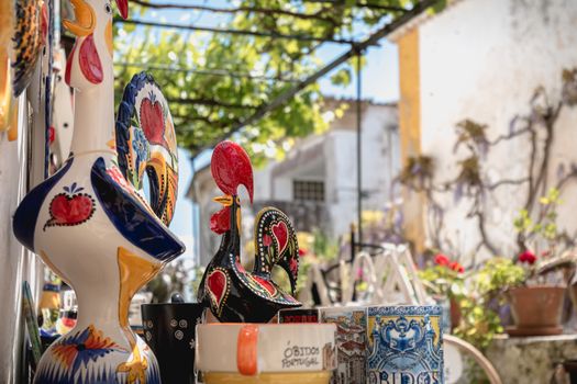 Obidos, Portugal - April 12, 2019: City rooster, cups, bowls and various souvenir items on the display of a souvenir shop in the historic city center on a spring day
