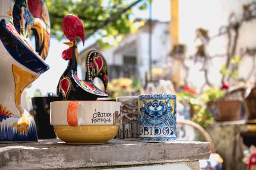 Obidos, Portugal - April 12, 2019: City rooster, cups, bowls and various souvenir items on the display of a souvenir shop in the historic city center on a spring day