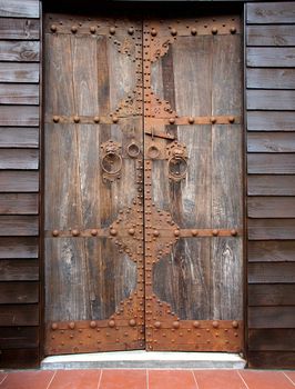 Large wooden door with bronze fittings and lion shaped door knockers
