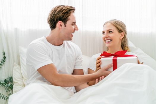 Caucasian Happy couple of lovers is celebrating together on the bedroom in home, Young woman is receiving her boyfriend a gift box for surprise, surprise for valentine or anniversary or christmas.