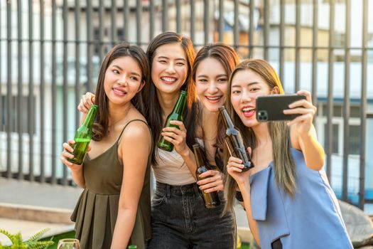 Happiness Asian Girl Friend Group taking a selfie while celebrating and dancing together with her beer bottle at sunset time on rooftop, hens night, holiday, or yearly anniversary party concept