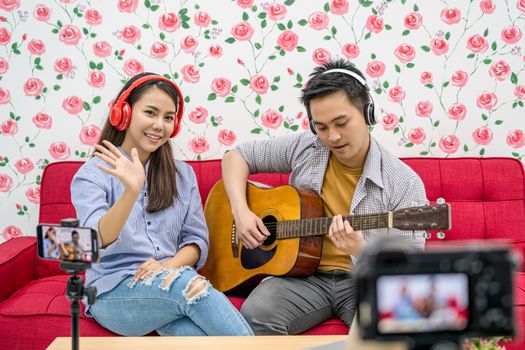 Asian Vlogger of married couple playing and sharing the music to attendee via mobile phone by social media channel, camera taking video and stream live, vlog and influencer freelance concept